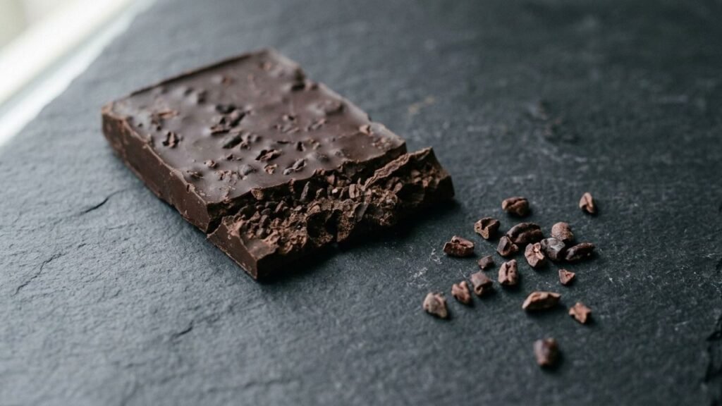 Broken dark chocolate bar showing irregular cocoa nibs embedded inside.